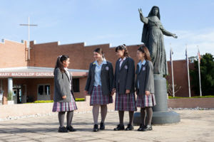 Four students talking in front of Mary MacKillop statue at Mary MacKillop Catholic College Wakeley